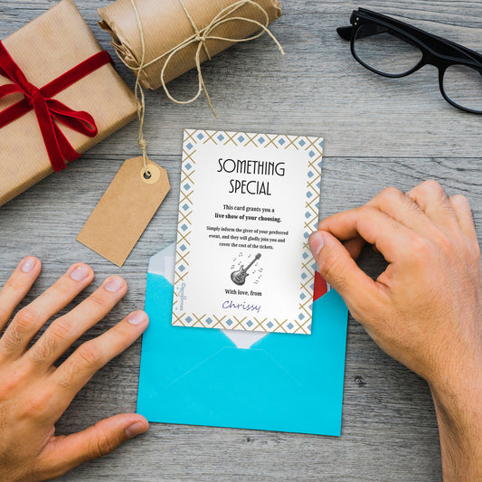 A person's hands are shown opening a bright blue envelope to reveal a 'Something Special' card. The scene is styled on a gray wooden tabletop with a brown gift box, a tag, a rolled piece of twine, and black eyeglasses.