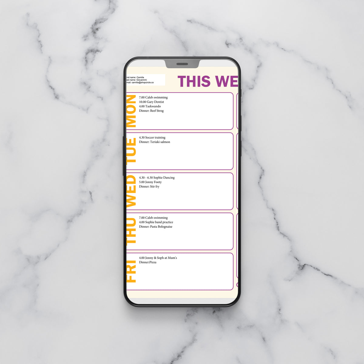 A smartphone lying on a white marble surface, displaying a weekly planner layout with the heading 'THIS WEEK' and vertical weekday labels in yellow. Some fields have been filled in with events.