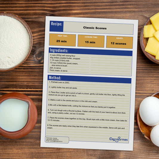 A recipe page template filled in with the recipe for Classic Scones, printed with blue, white, and orange sections, styled on a wooden table with baking ingredients like butter, flour, and eggs around it. The brand name 'DecoForms' is visible at the bottom right of the card.